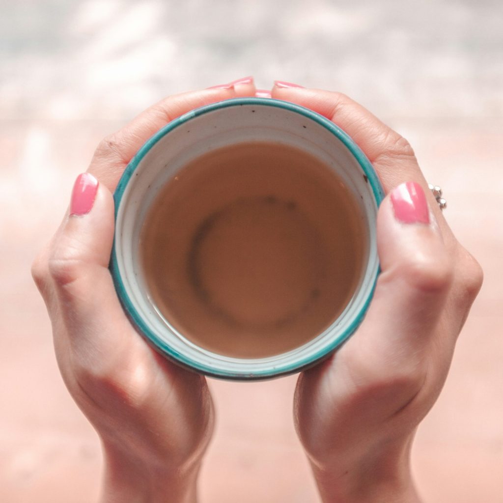 person holding blue ceramic mug with brown liquid